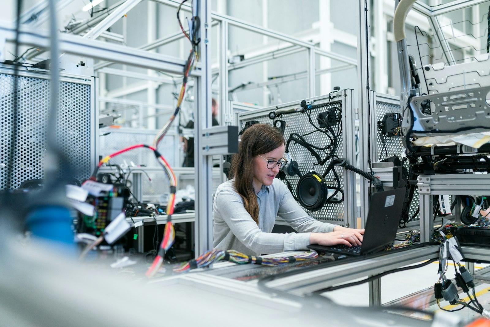 An engineer reviewing production data on a laptop beside automated equipment