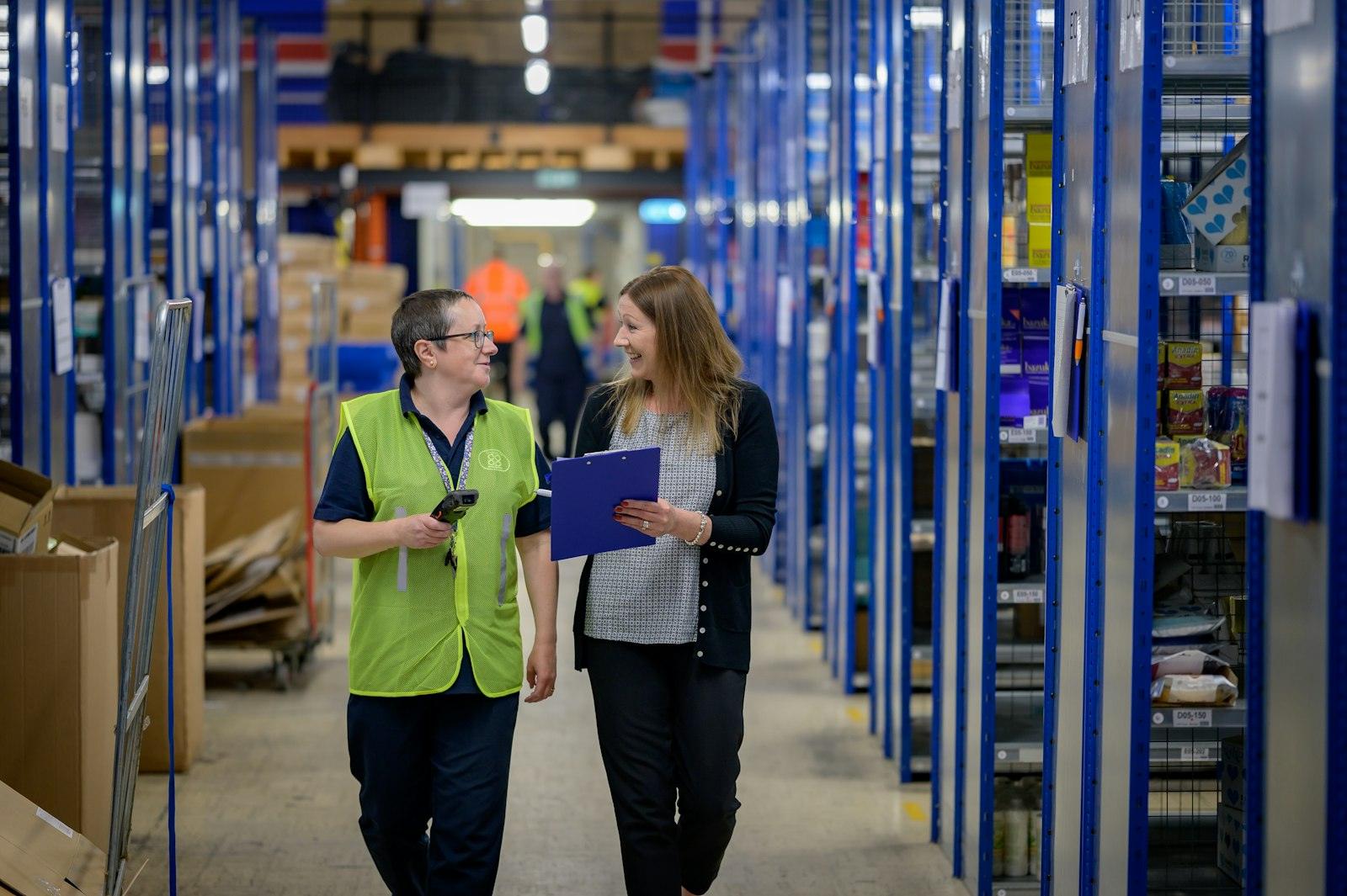 Two warehouse managers reviewing orders on a tablet between shelving